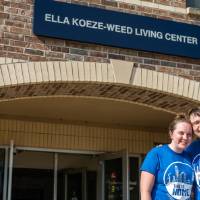Two alumni by Ella Koeze-Weed Living Center sign